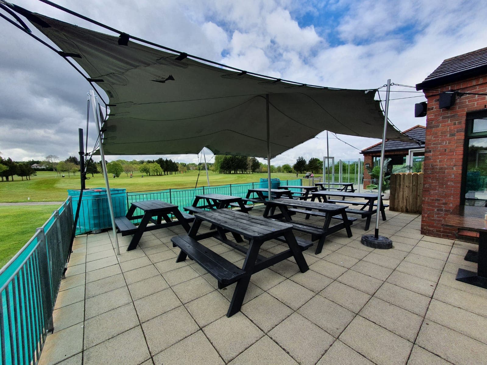 Stretch tent canopy covering picnic benches on a terrace beside a brick clubhouse overlooking a golf course
