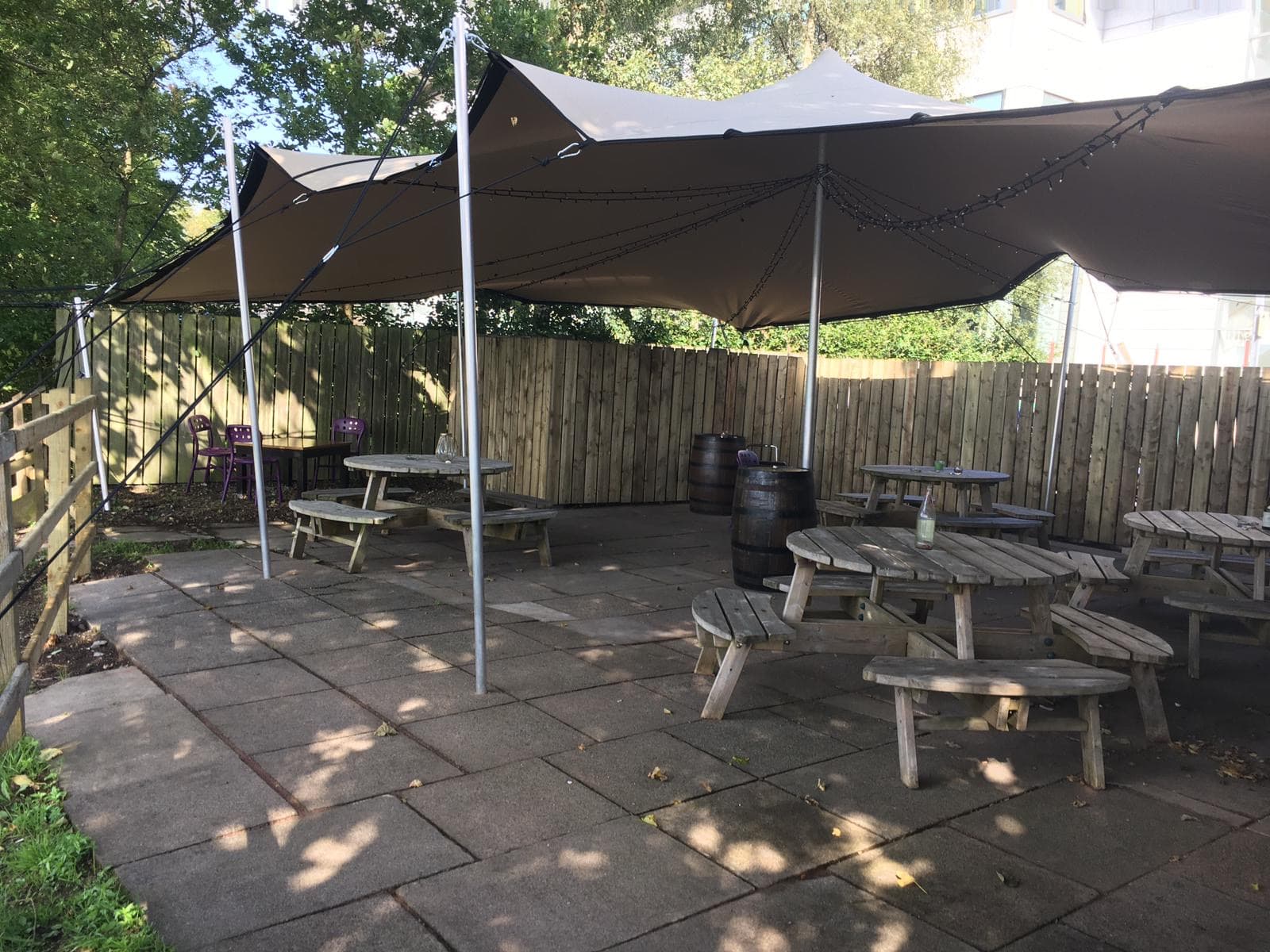 Stretch tent covering an outdoor pub-style seating area with picnic benches and festoon lighting