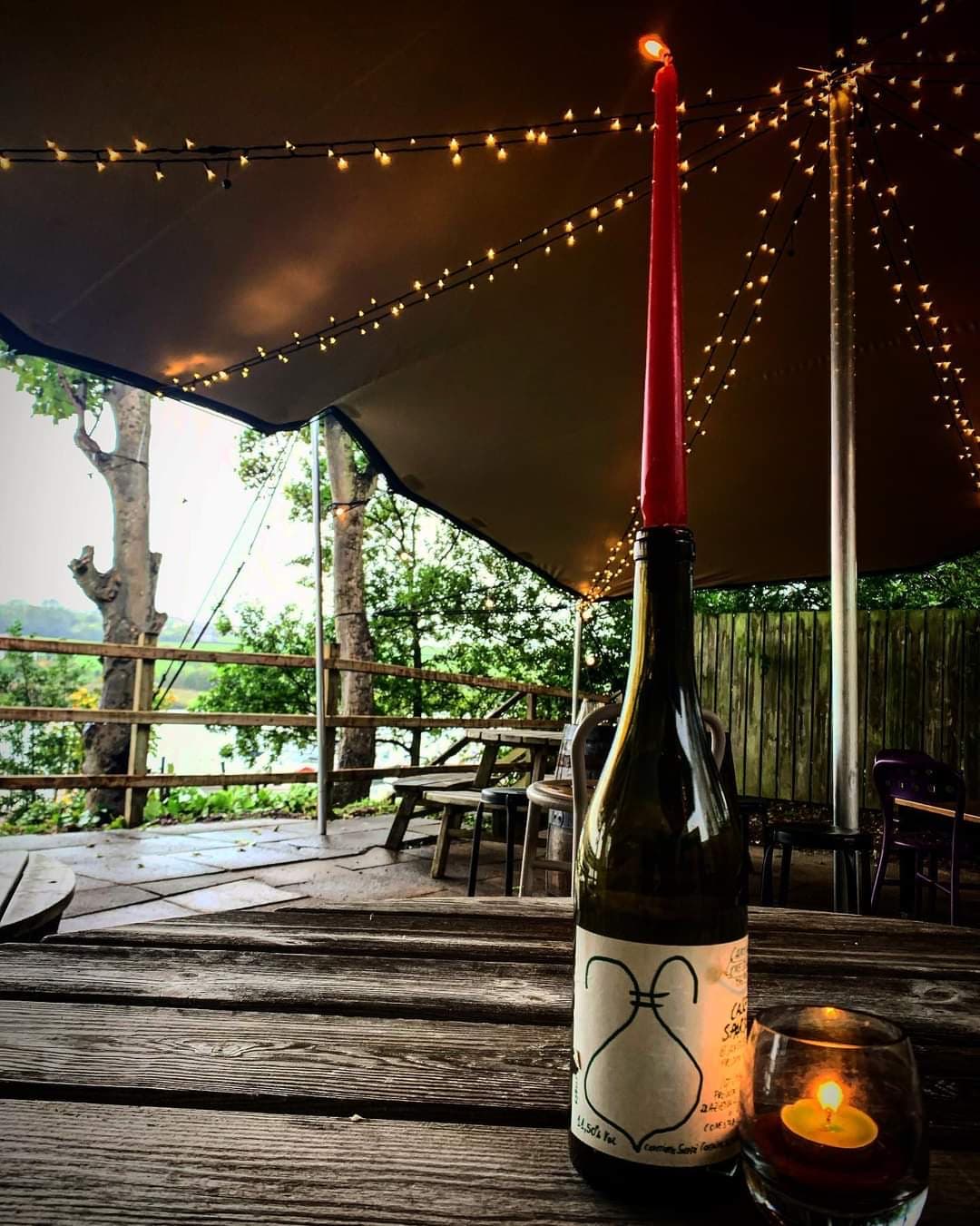 Cosy stretch tent interior with festoon lights, a wine bottle candle and a glowing tealight on a rustic wooden table