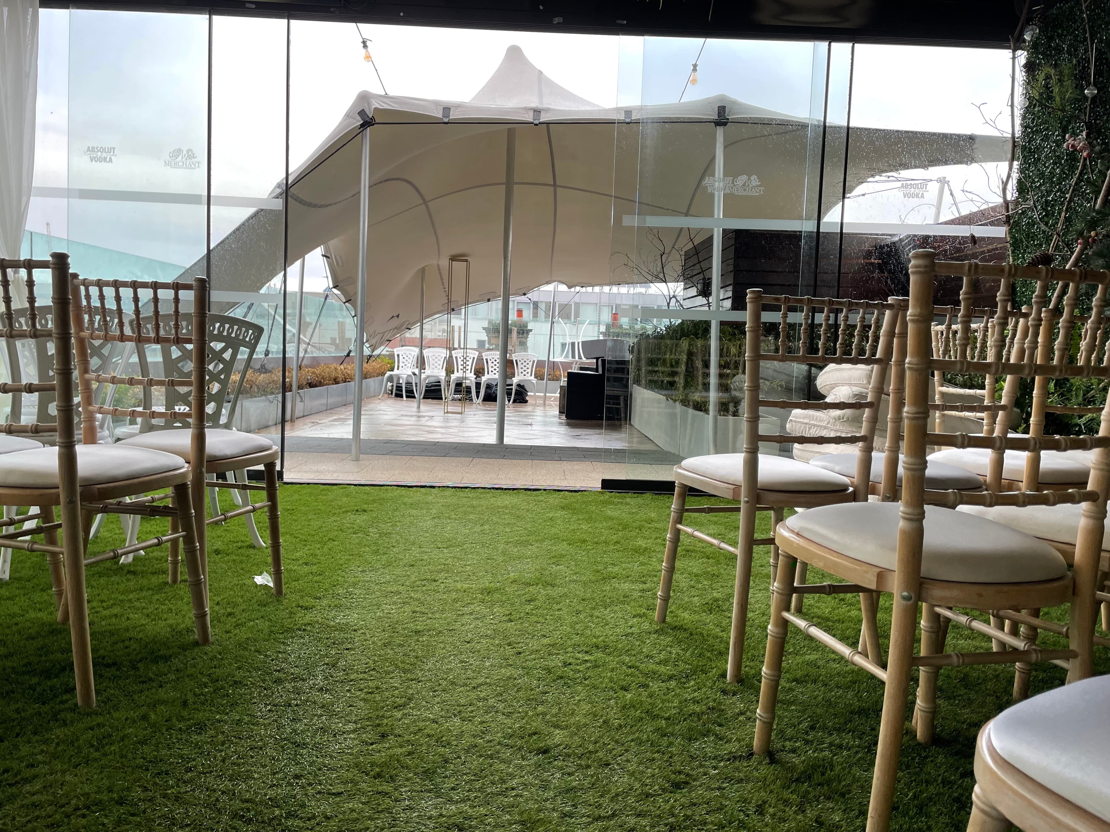Indoor seating area with chiavari chairs looking out through glass to a white stretch tent on an outdoor terrace