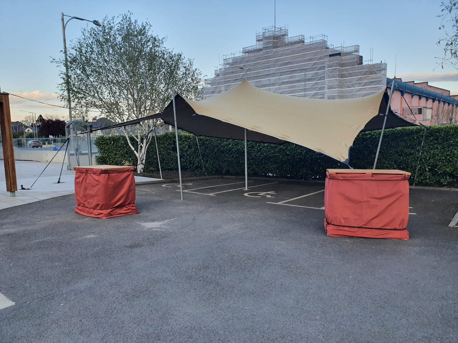 Stretch tent installed over a paved outdoor area beside hedges and a building