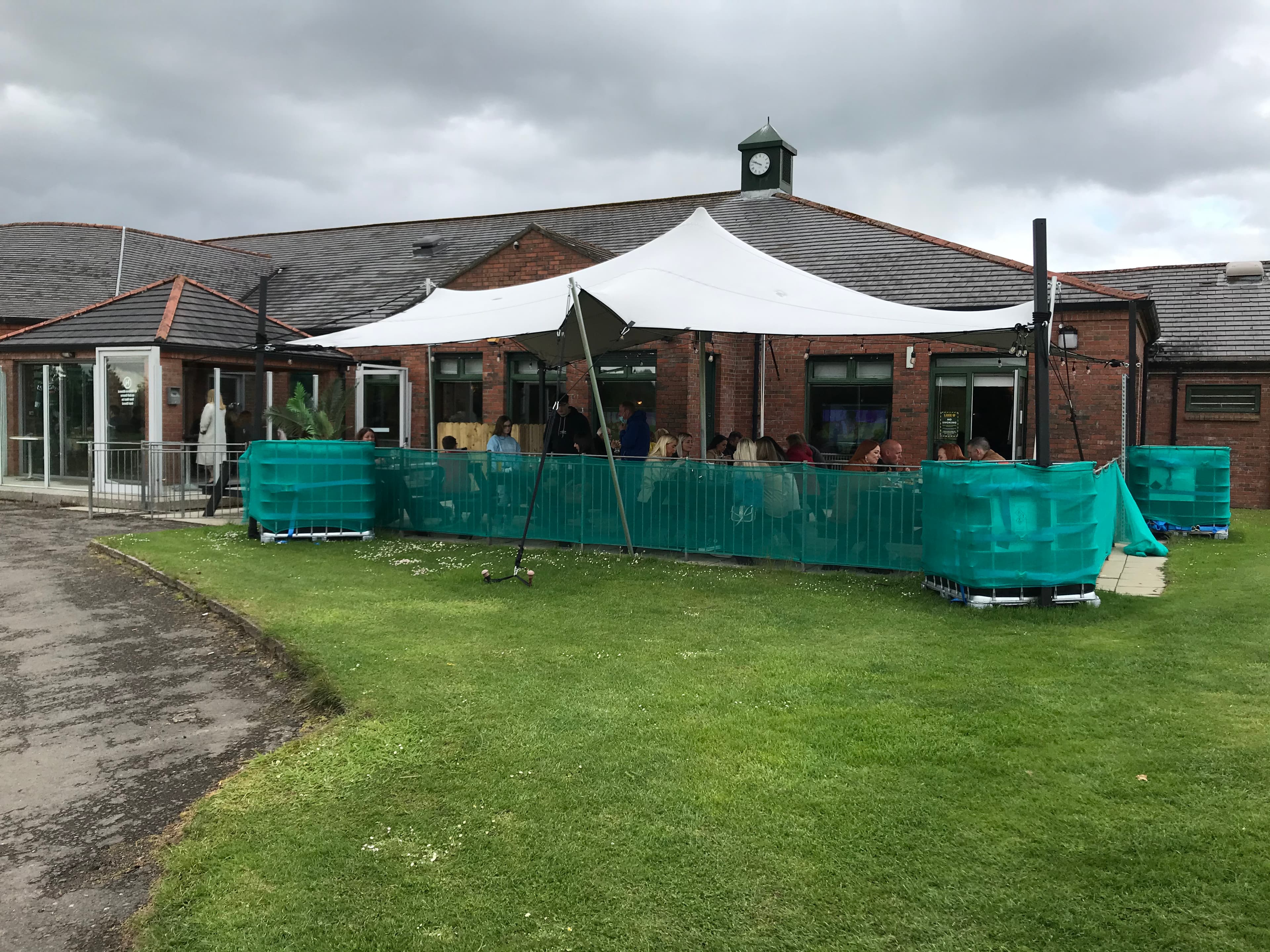 White stretch tent covering an outdoor seating area beside a brick venue under cloudy skies