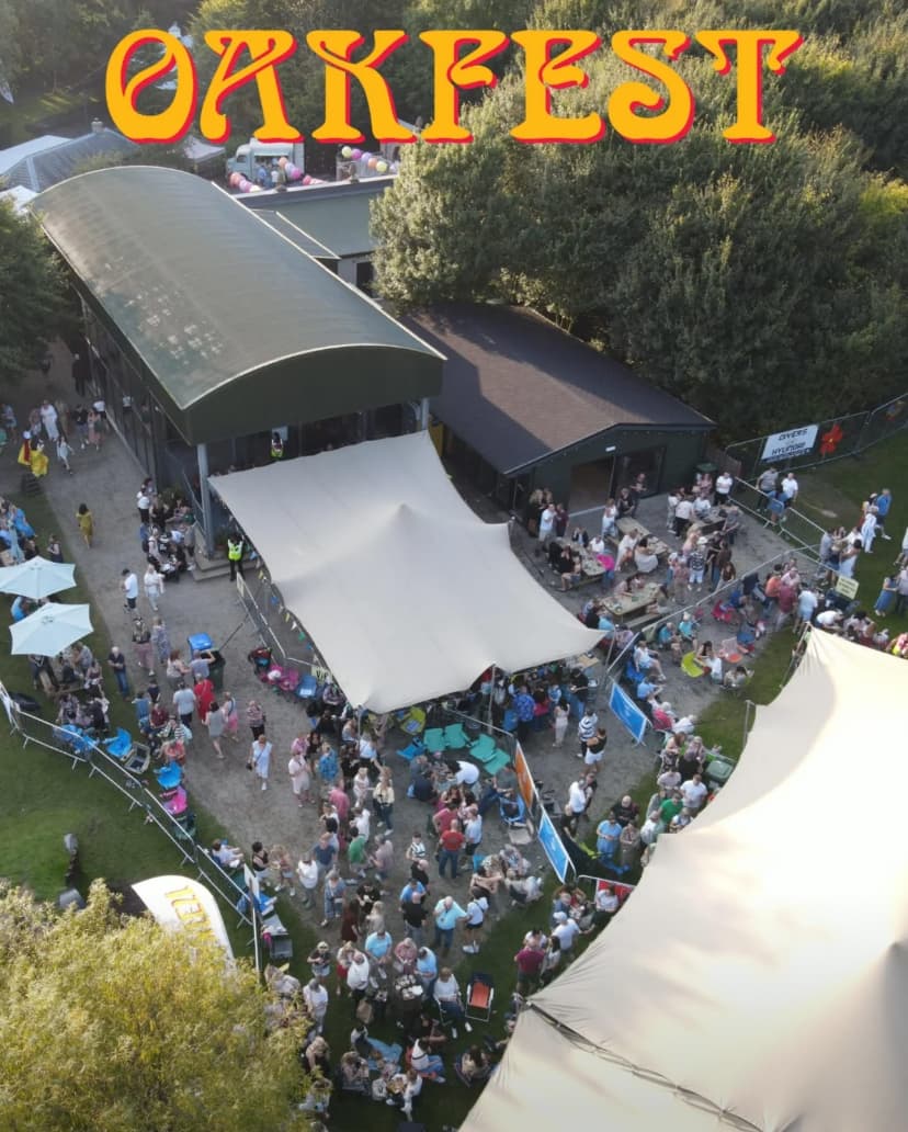 Aerial view of a busy outdoor festival with stretch tents beside a large venue building and trees, with OAKFEST text overlaid