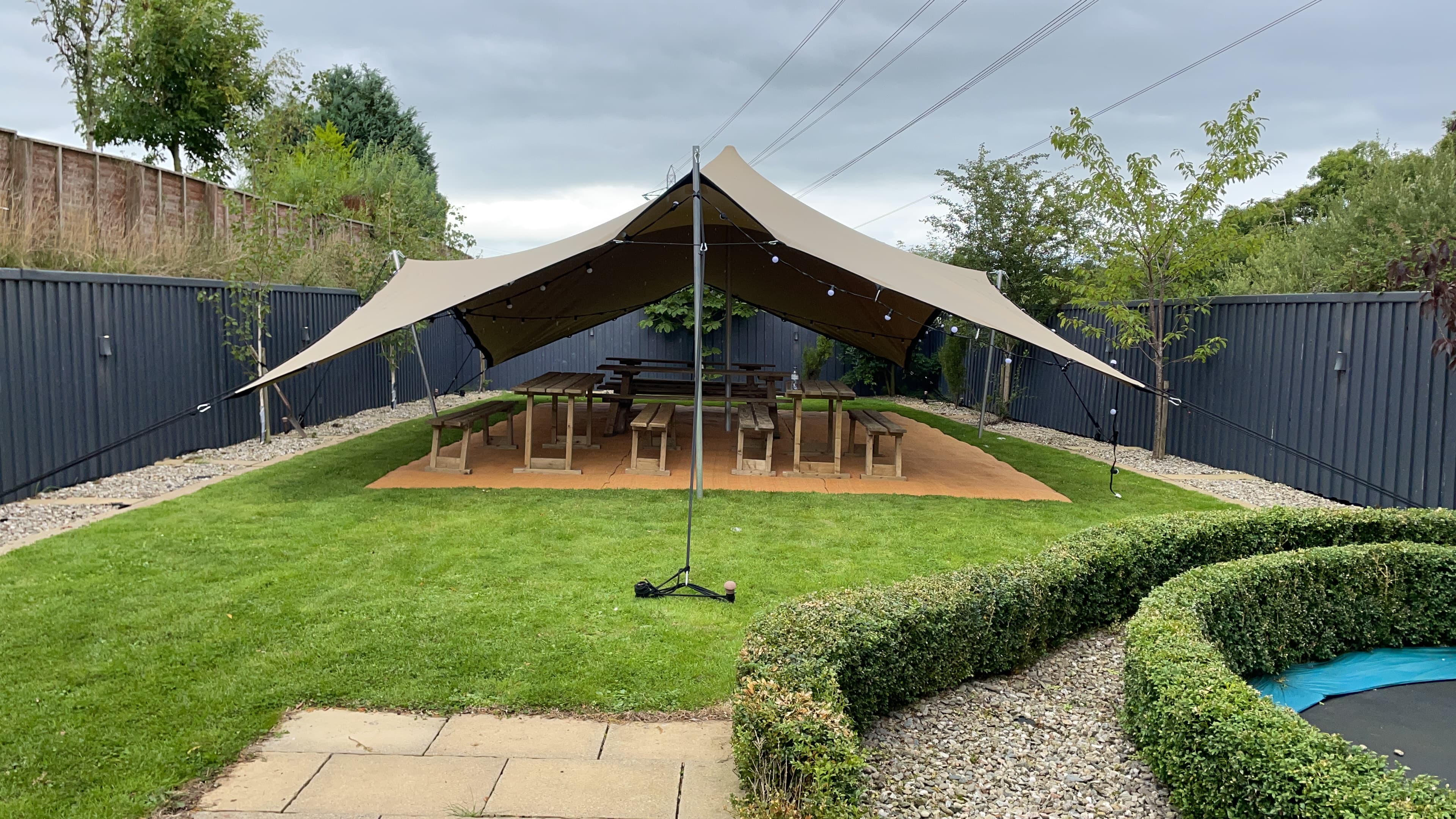 Stretch tent set up in a landscaped back garden with picnic benches underneath