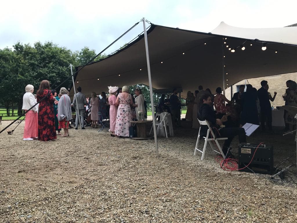 Guests gathered beneath a stretch tent at an outdoor wedding reception with festoon lights overhead