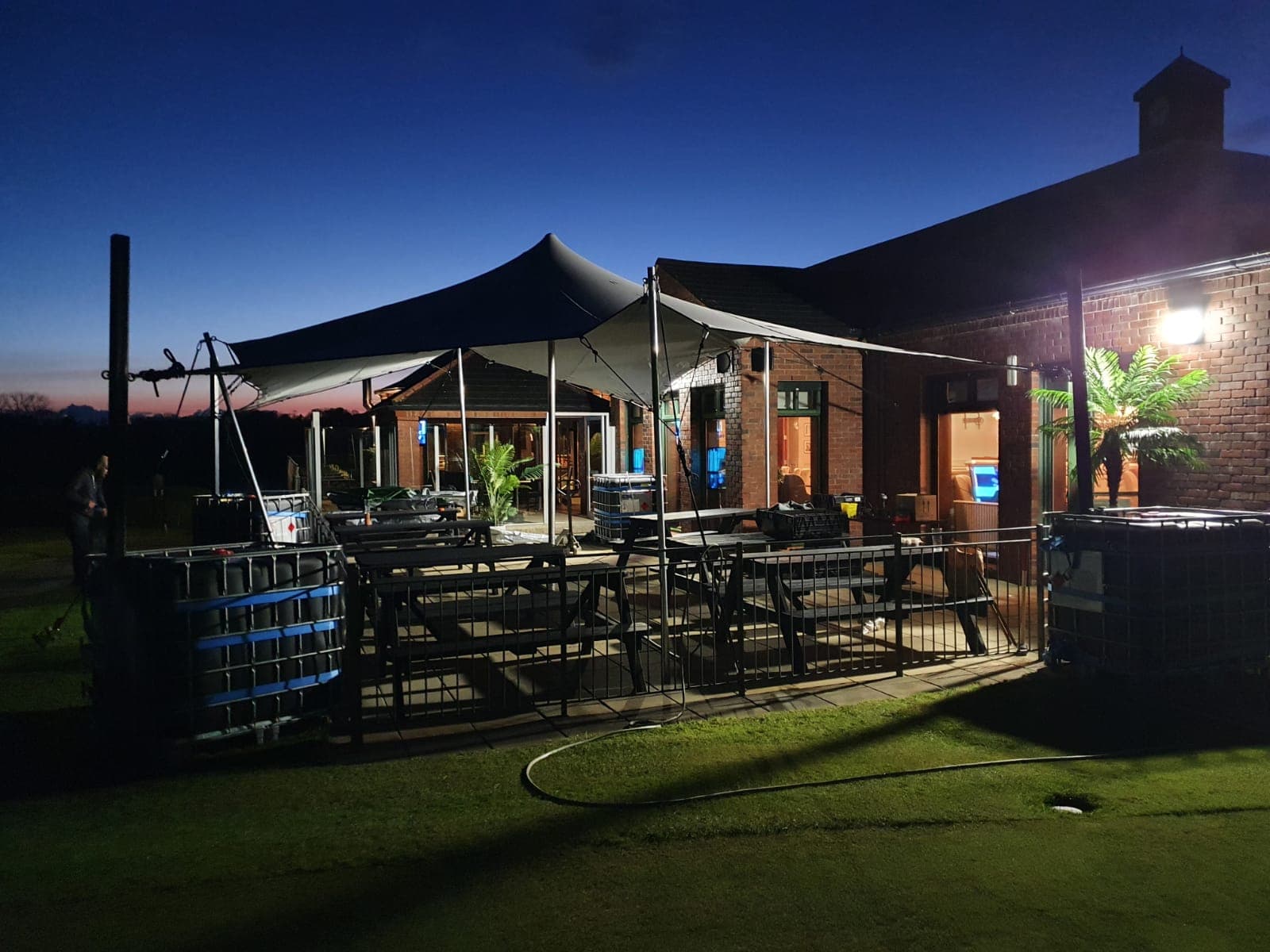 Stretch tent installed over an outdoor patio beside a brick clubhouse at dusk