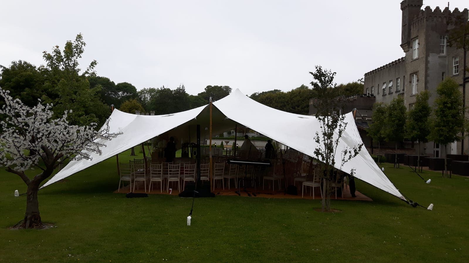 White stretch tent set up on a lawn beside a historic stone building with chairs arranged underneath