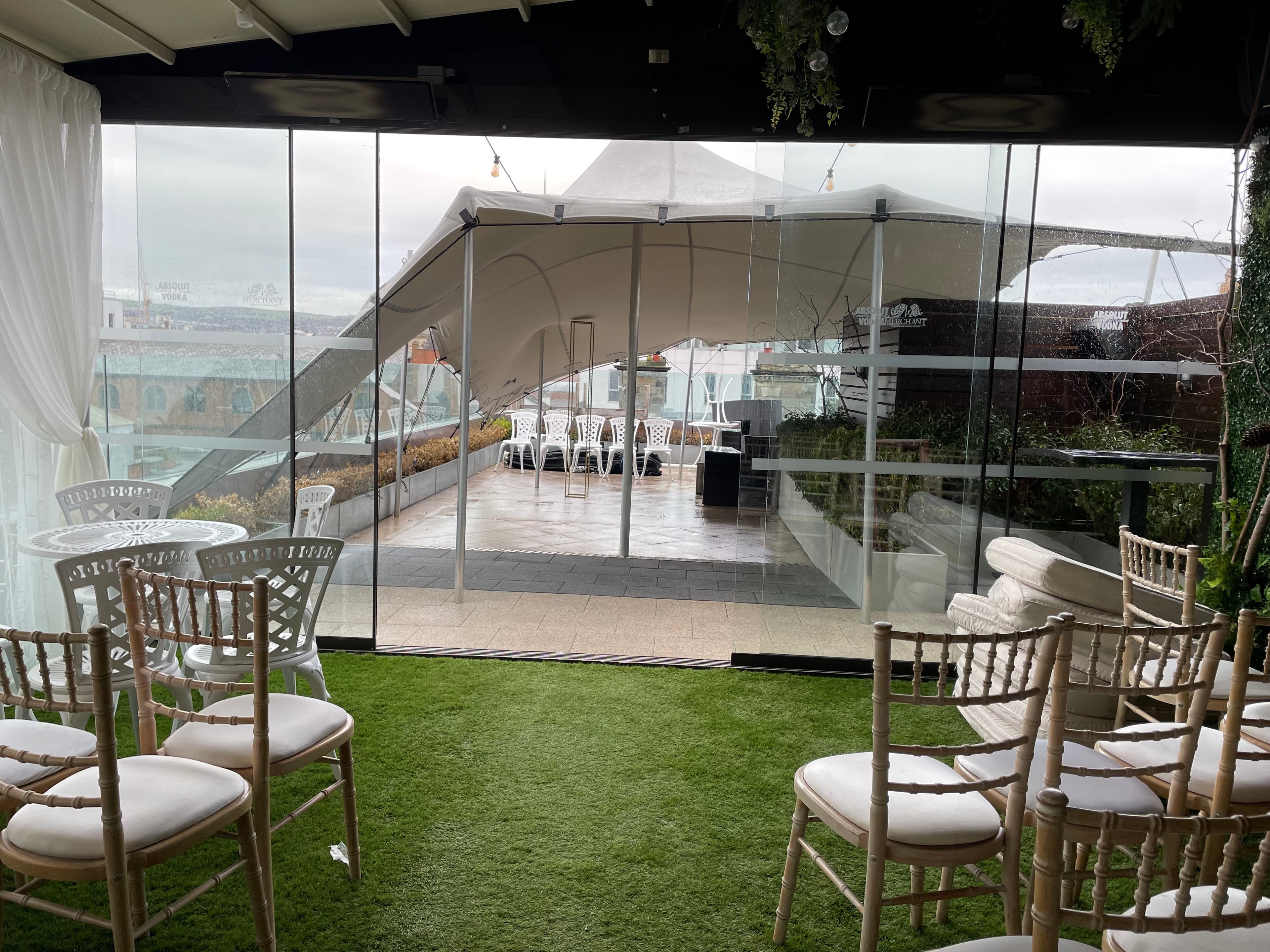 View from an indoor lounge toward a white stretch tent covering a rooftop terrace set for an event