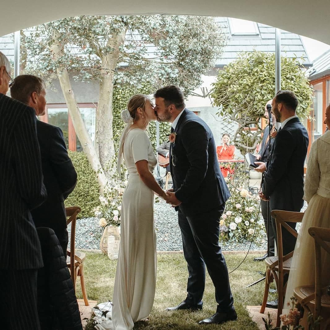 Bride and groom kiss during an intimate wedding ceremony beneath a stretch tent